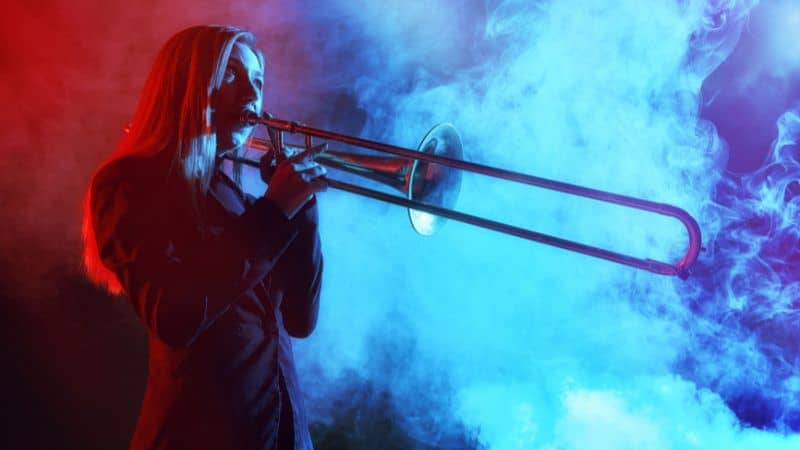 A person plays a trombone onstage surrounded by red and blue smoke.