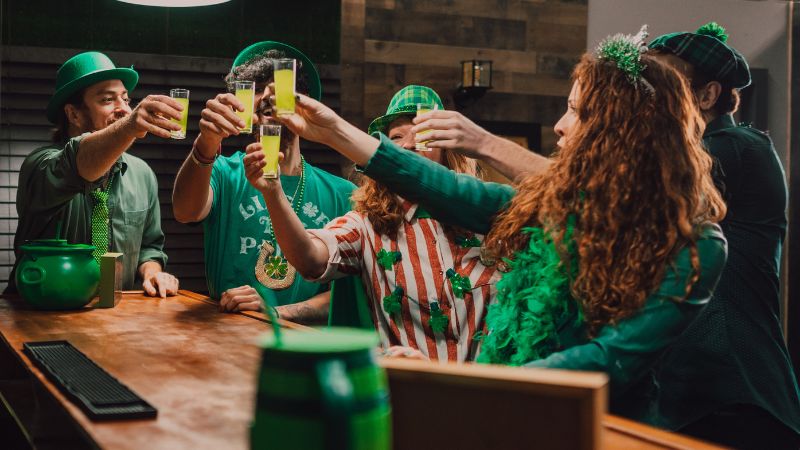 Group of people wearing green celebrate with drinks at a bar during a St. Patrick’s Day bar crawl.
