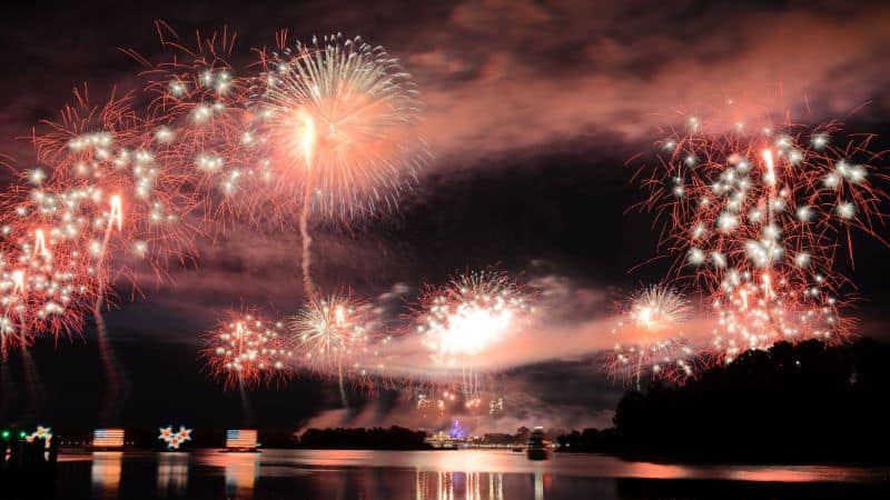Bright fireworks explode in the night sky above water.