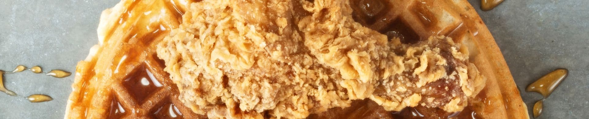 A piece of fried chicken on a waffle drizzled with syrup.