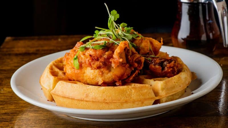 Fried chicken on waffles garnished with fresh herbs on a white plate.