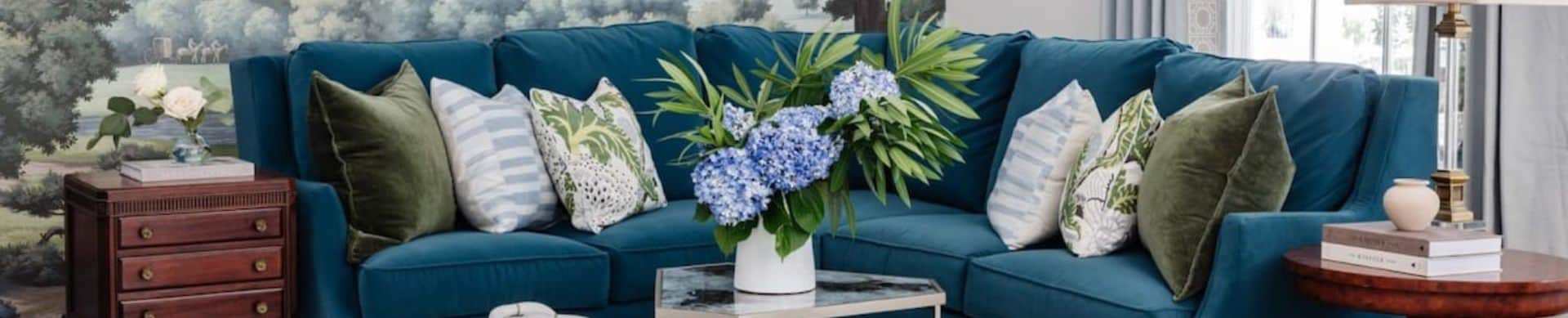 Teal sectional sofa with assorted pillows and a vase of blue hydrangeas on a coffee table.