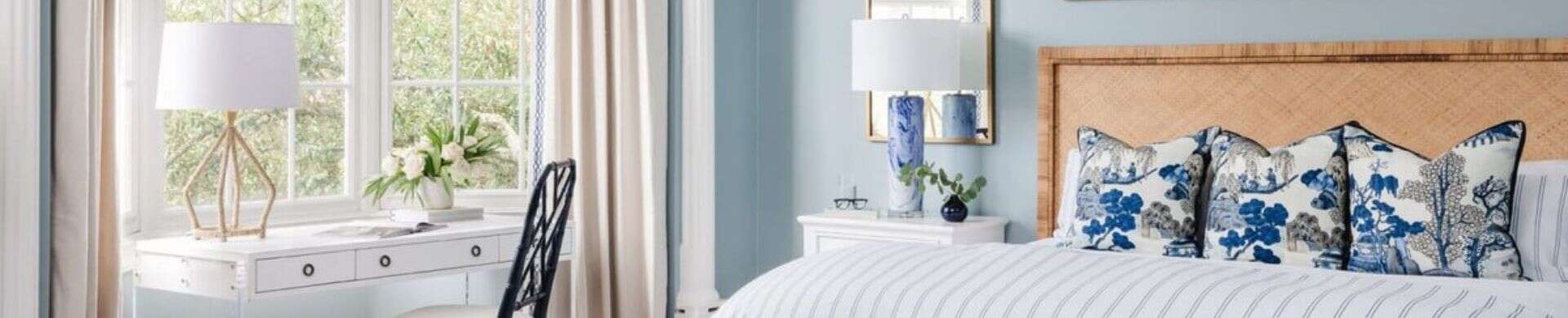 Bedroom with light blue walls, a wicker headboard, and blue-patterned pillows.