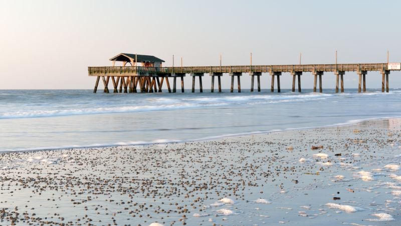 Wooden pier extending into the ocean along a quiet sandy beach.