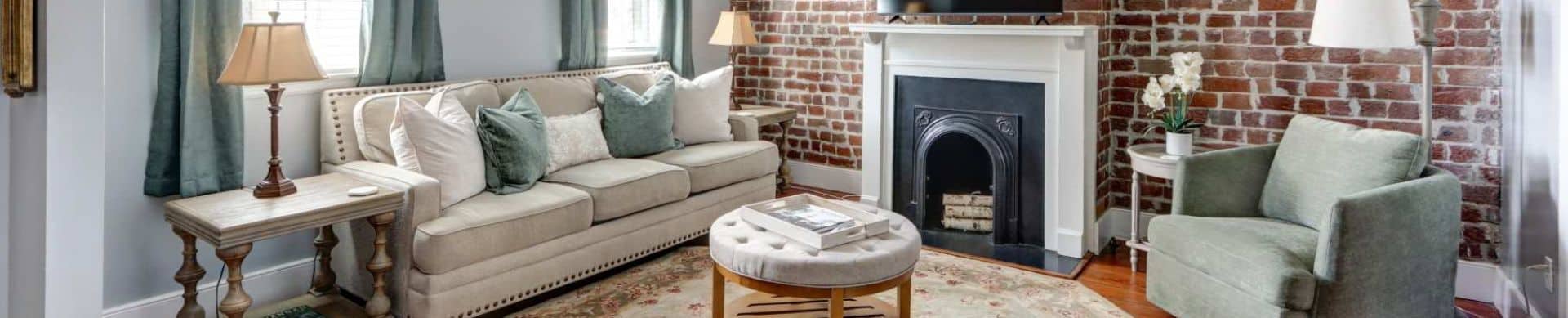 Cozy living room with a beige sofa, green armchair, brick accent wall, and decorative fireplace.
