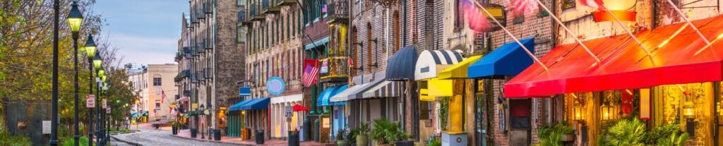 Historic Savannah street with brick buildings, striped awnings, and glowing storefront lights.