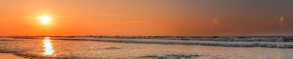 Bright orange sunrise over ocean waves along a sandy shoreline.