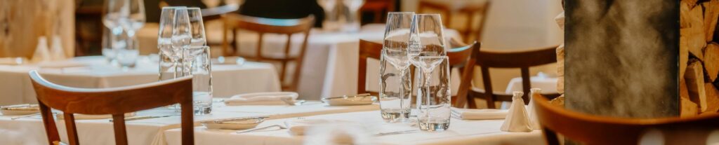 Elegant restaurant tables set with white tablecloths, wine glasses, and wooden chairs.