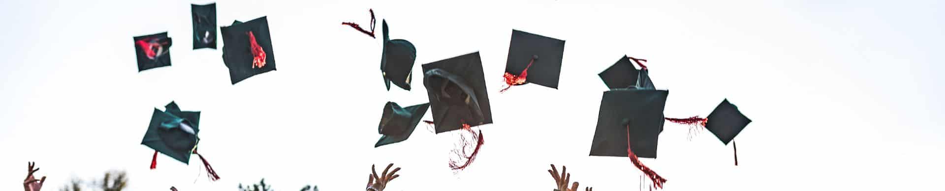 Graduates tossing black mortarboard caps with red tassels into the sky.