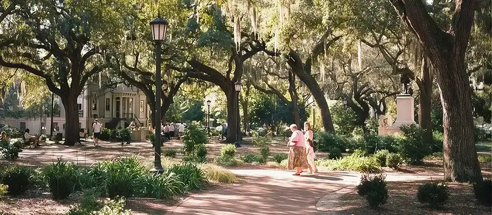 Visitors walking a shaded path under oak trees draped in Spanish moss in a Savannah square